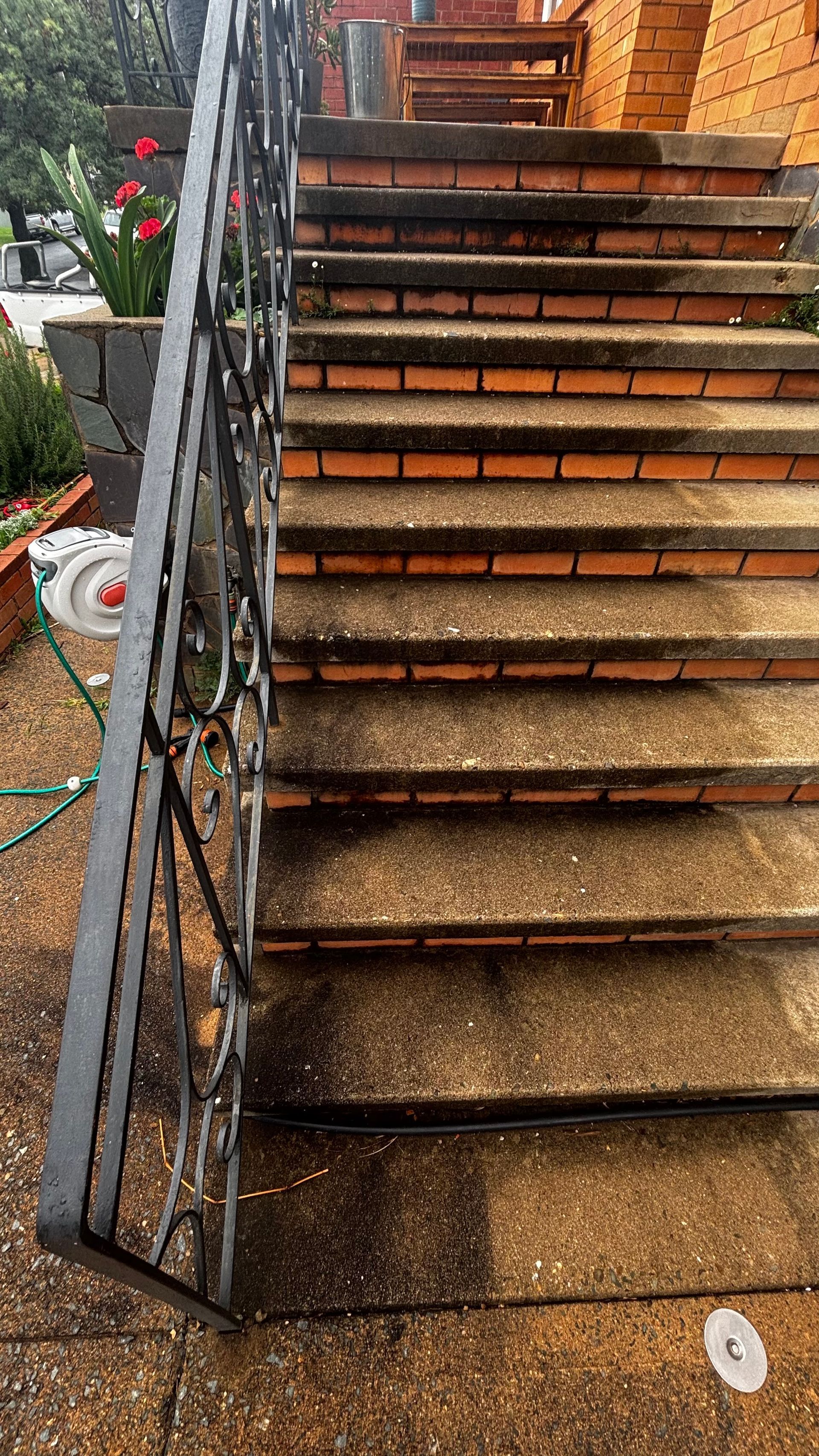 Rusted outdoor metal staircase with black railing beside a brick building and wet steps from rain