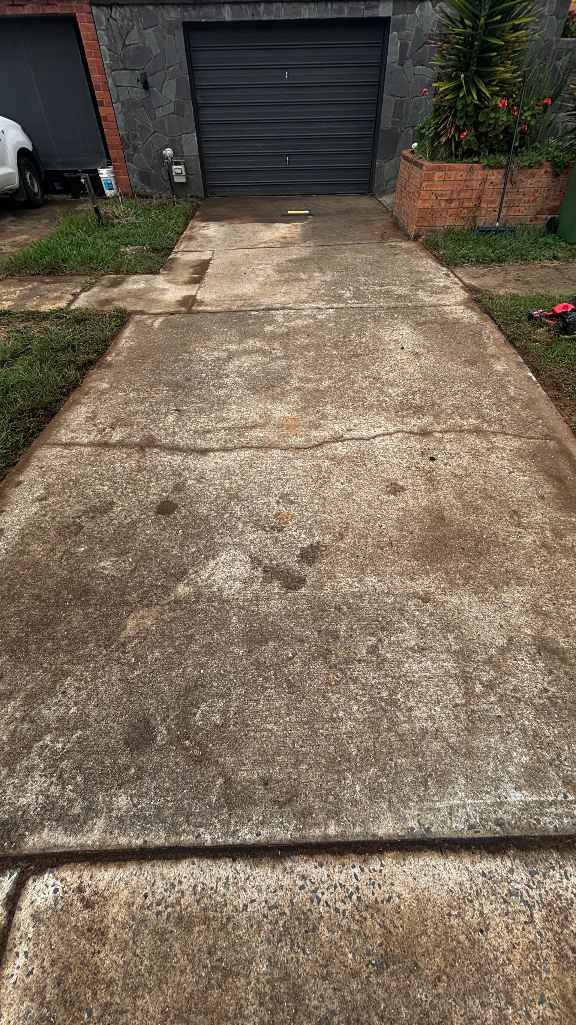Concrete driveway leading to a black garage door beside a brick house and garden wall