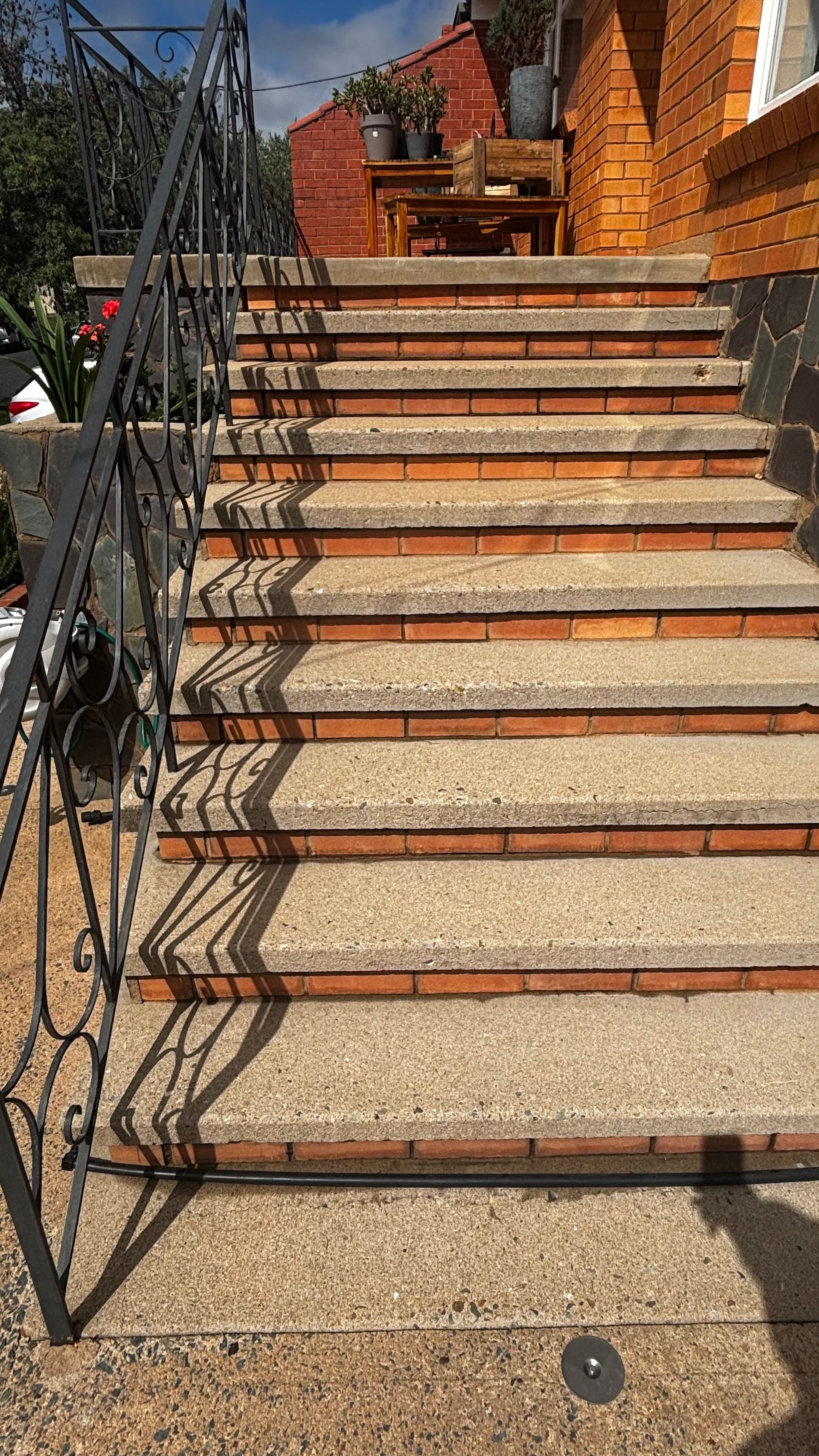 Outdoor brick staircase with ornate black iron railing, leading up beside a brick wall and flowers.