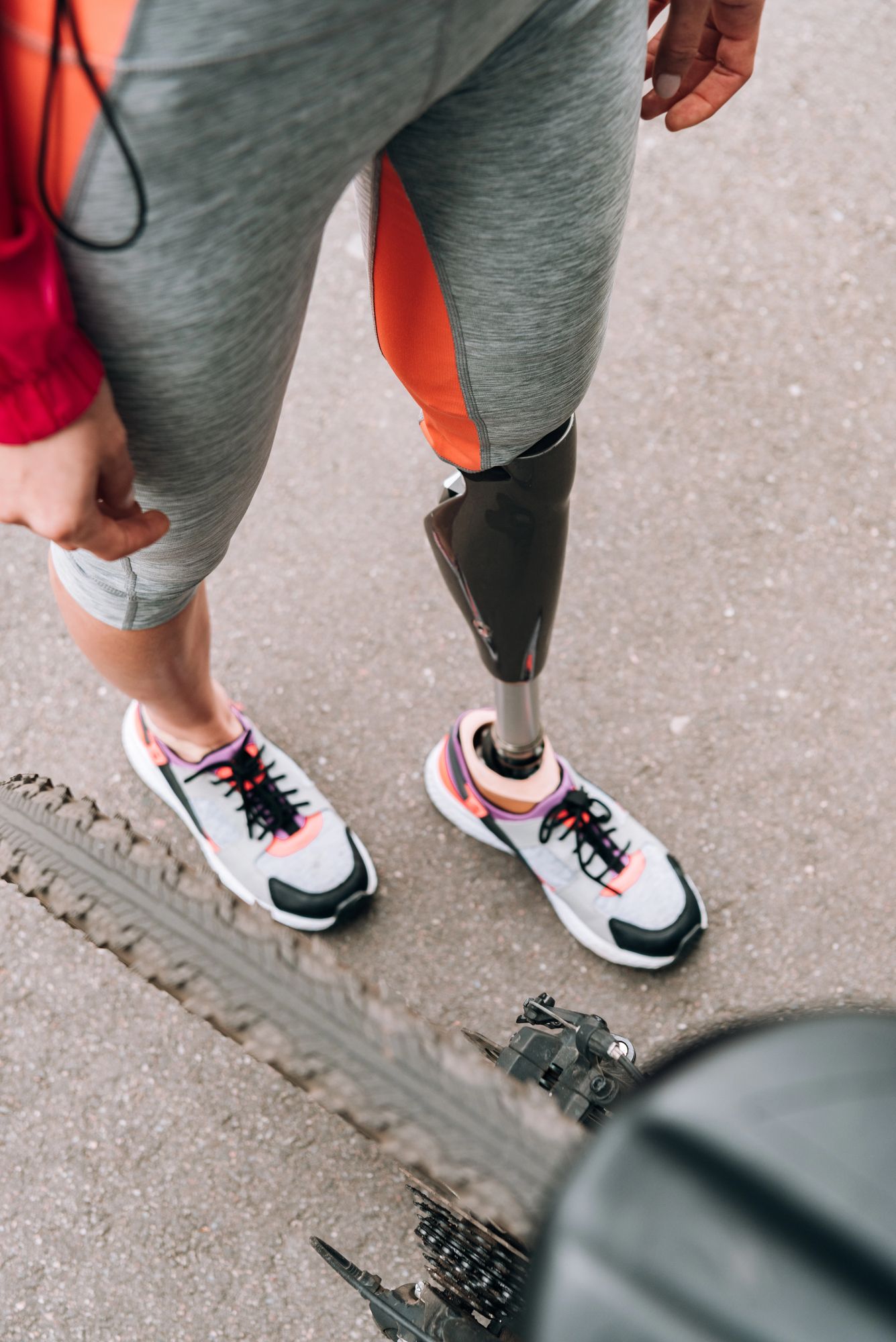 Uomo con una protesi nera alla gamba che cammina su un sentiero lastricato indossando pantaloncini grigi e scarpe da ginnastica bianche.