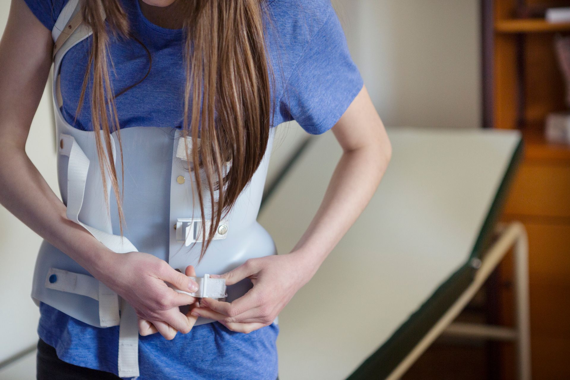 In un ambulatorio, una persona si sistema un corsetto ortopedico bianco sopra una camicia blu.