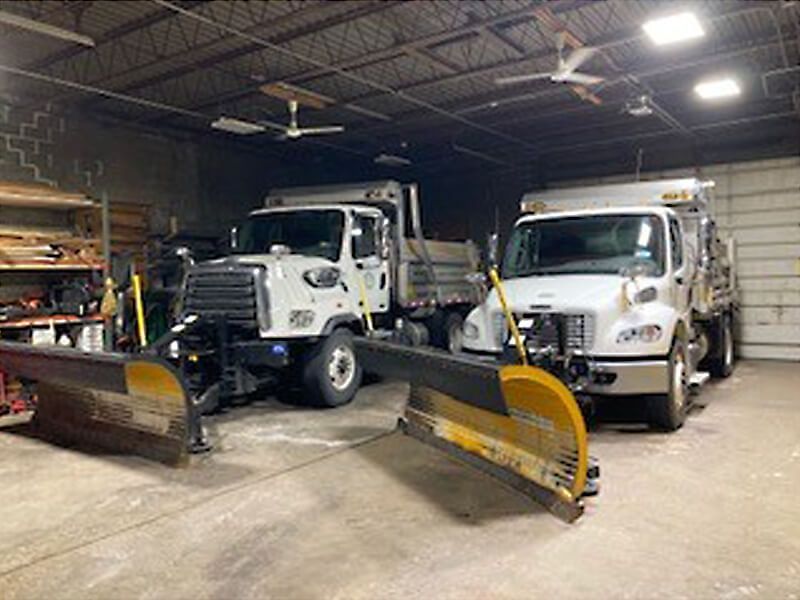 Two snow plows are parked in a garage next to each other.