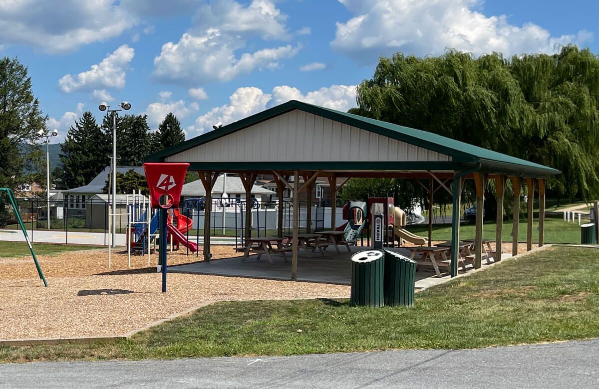 A picnic shelter in a park with a playground in the background.