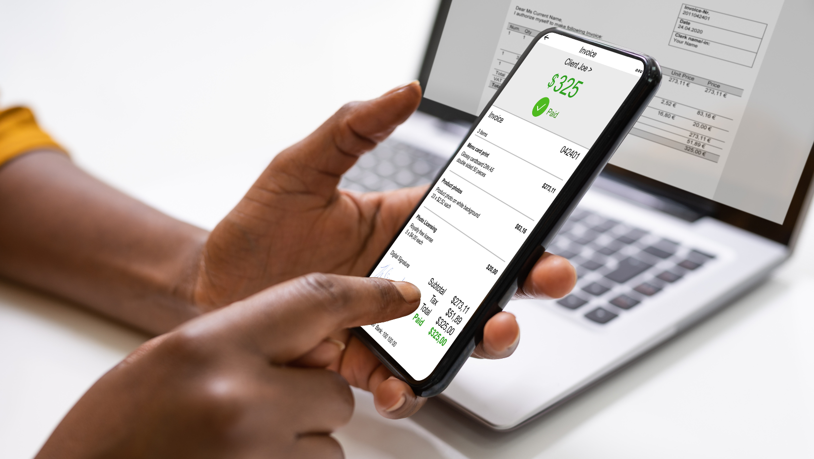 A person is holding a cell phone in front of a laptop.