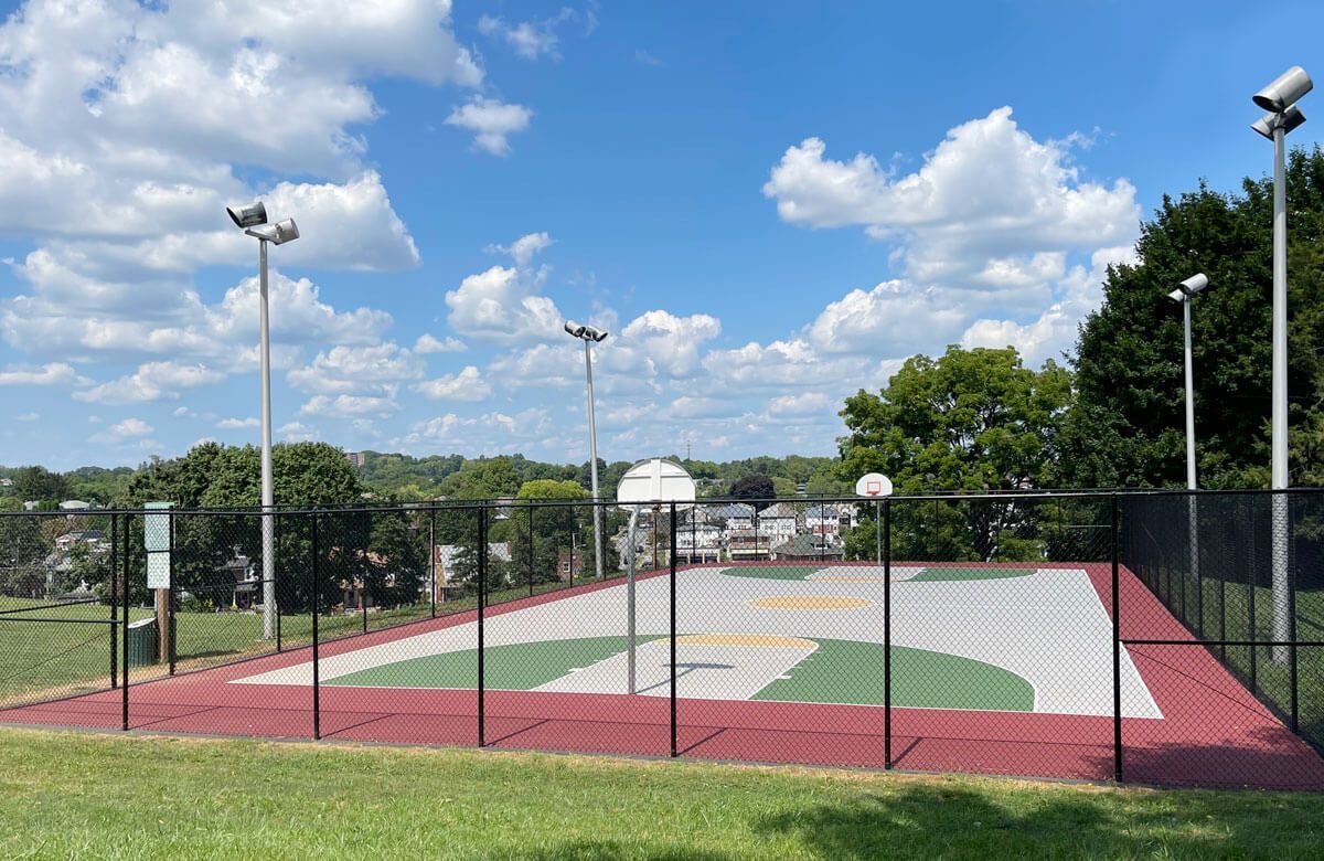 A basketball court in a park with a fence around it.