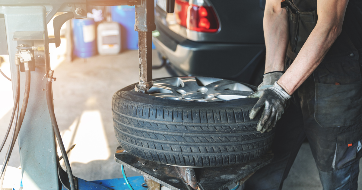 Mechanic wearing gloves lifts a car tire in a garage beside a vehicle. | European Autowerks – Virginia Beach