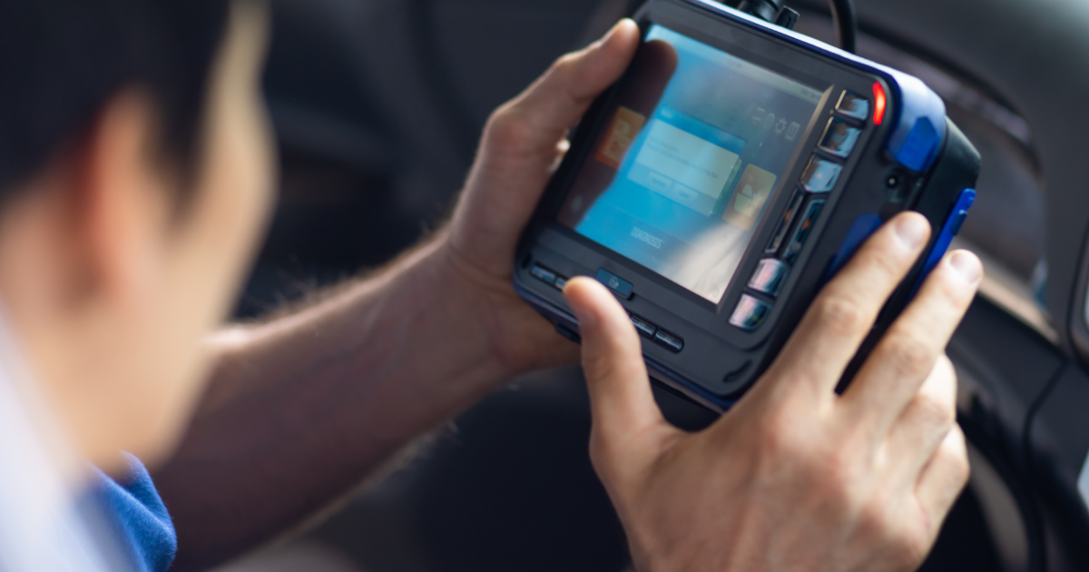Hands holding a rugged handheld device with a bright screen inside a vehicle | European Autowerks – Virginia Beach
