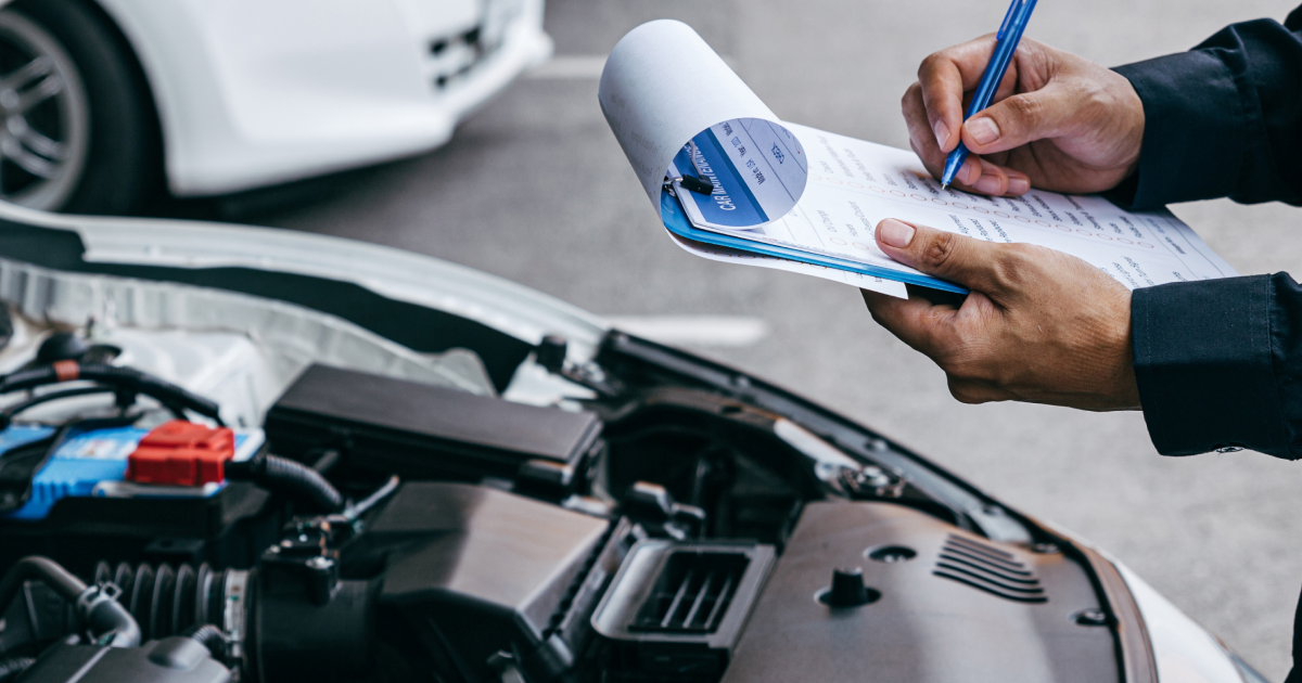 Mechanic writing on a clipboard beside an open car hood during a vehicle inspection | European Autowerks – Virginia Beach