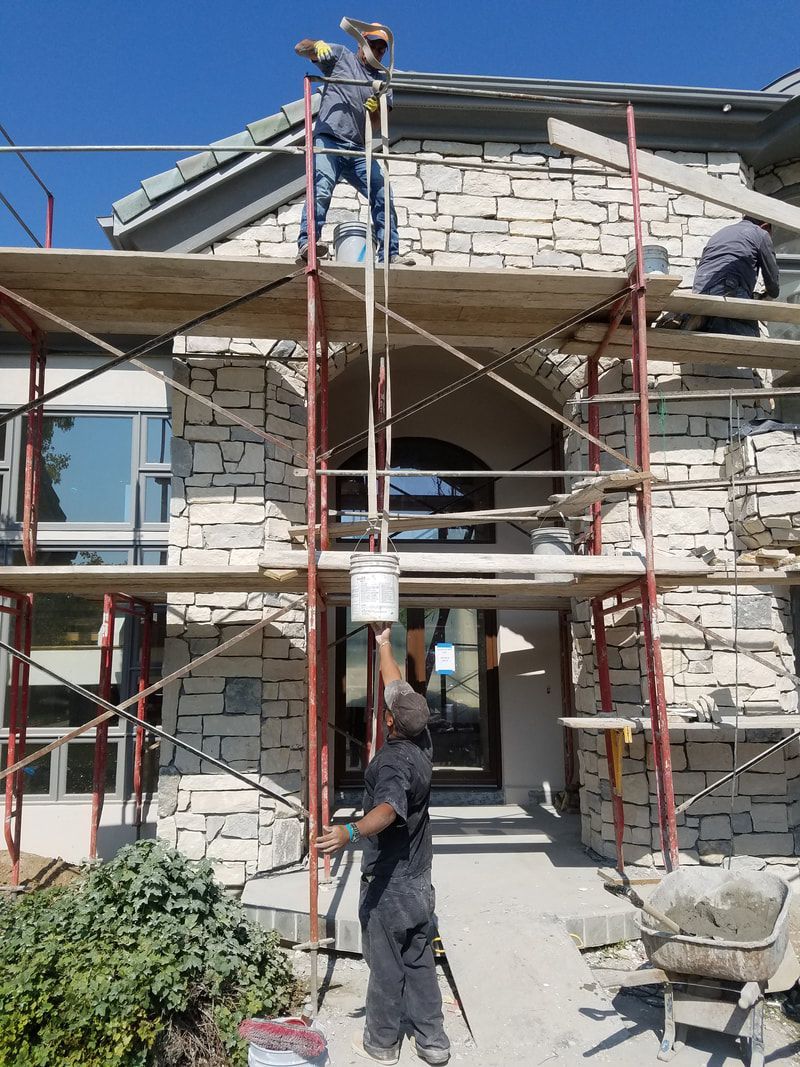 A man is standing on a scaffolding in front of a stone building