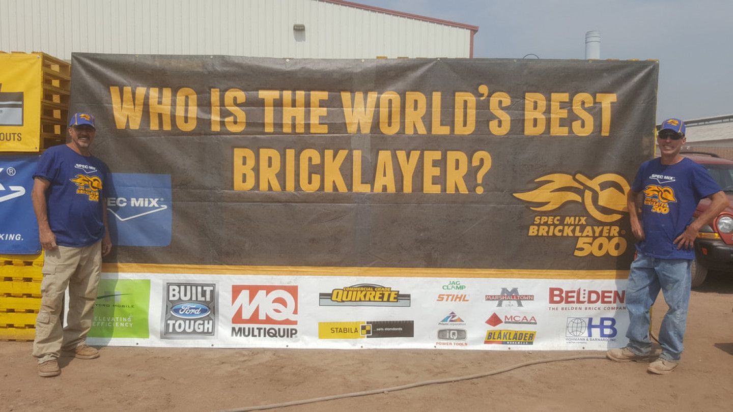 Two men standing in front of a banner that says who is the world 's best bricklayer