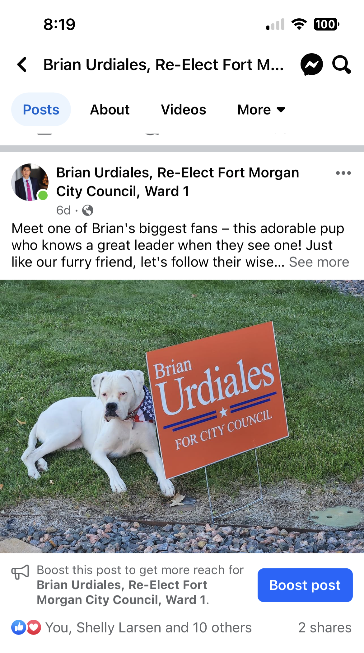 Dog beside a red “Urdiales” campaign sign on grass, with a Facebook post screenshot behind it