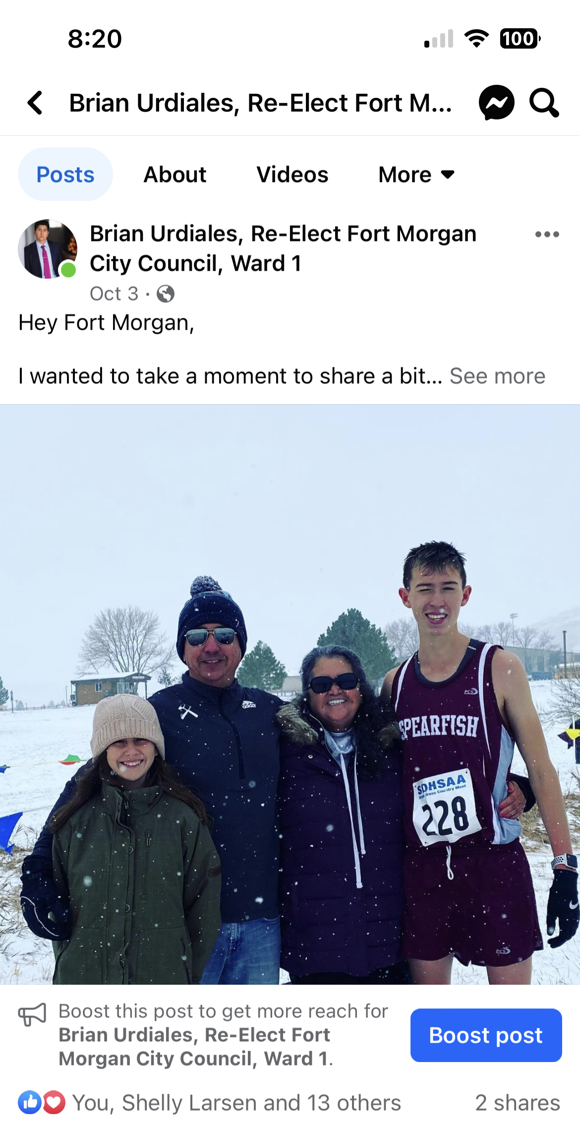 Four people in winter clothes stand outdoors in snow, with one wearing a maroon race bib.