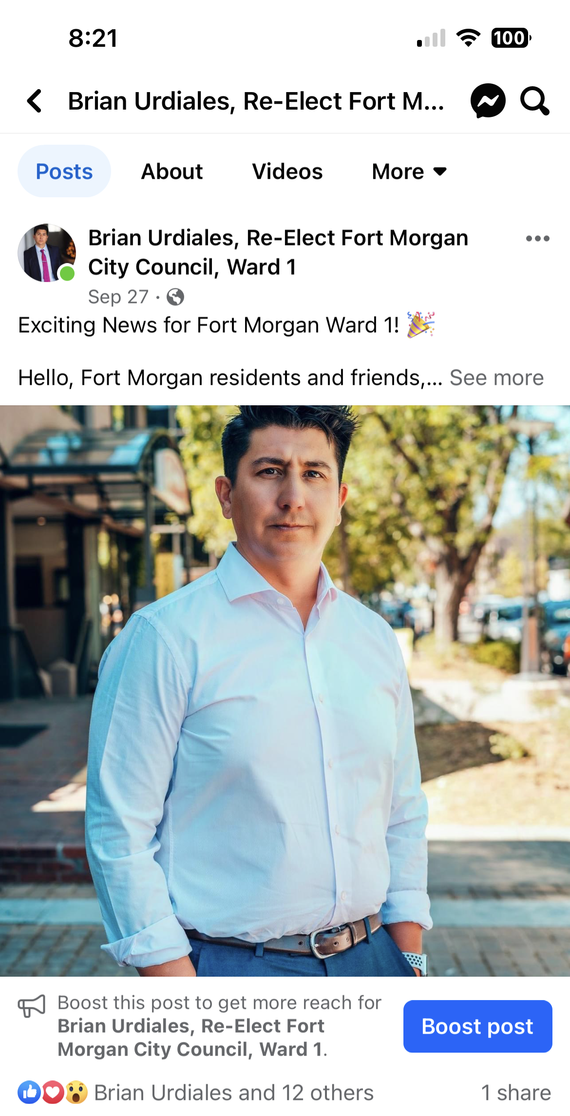 Brian Urdiales stands outdoors in a light blue shirt, with a city street and trees in the background.