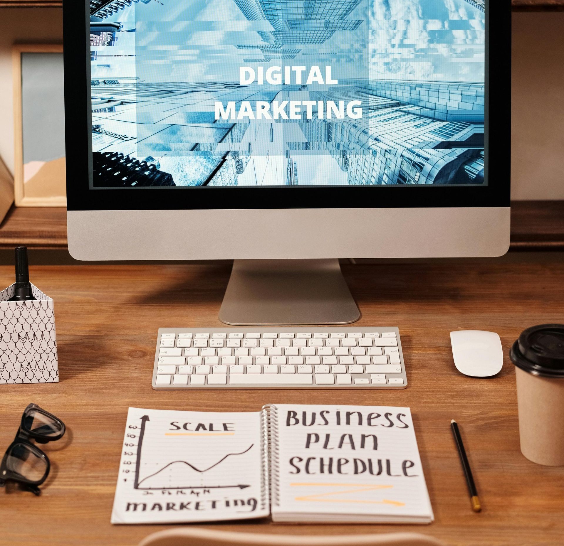Desktop workspace with monitor displaying “Digital Marketing,” keyboard, notebook, and coffee cup on wooden desk
