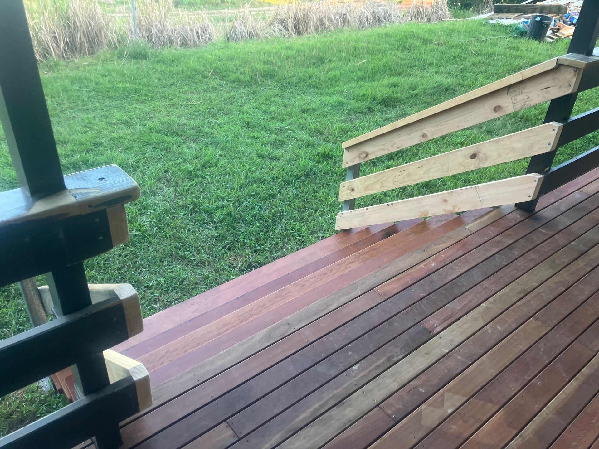 Wooden porch deck with stairs railing, overlooking a grassy yard.