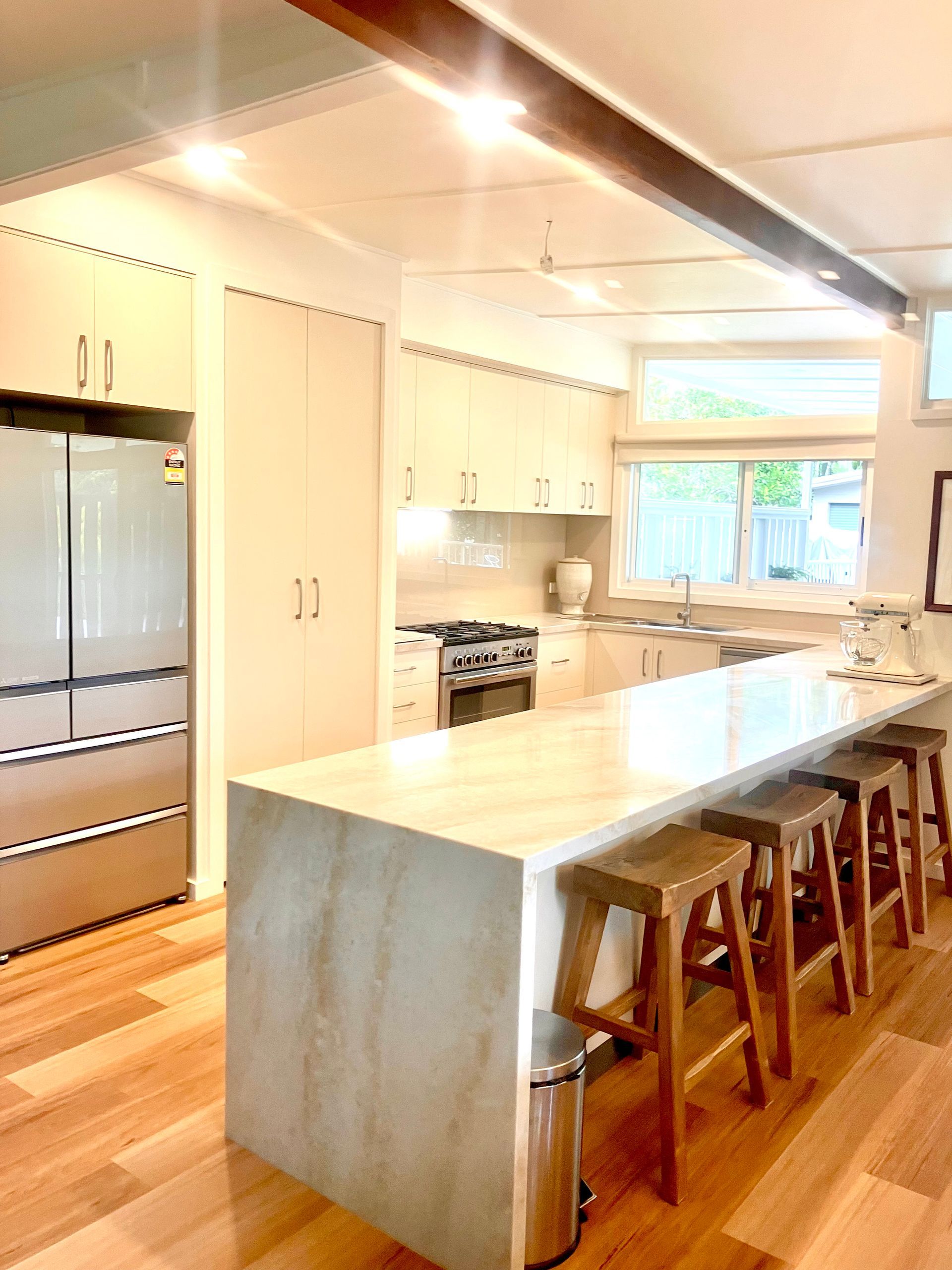 Bright modern kitchen with stainless fridge, white cabinets, marble island, and wooden stools