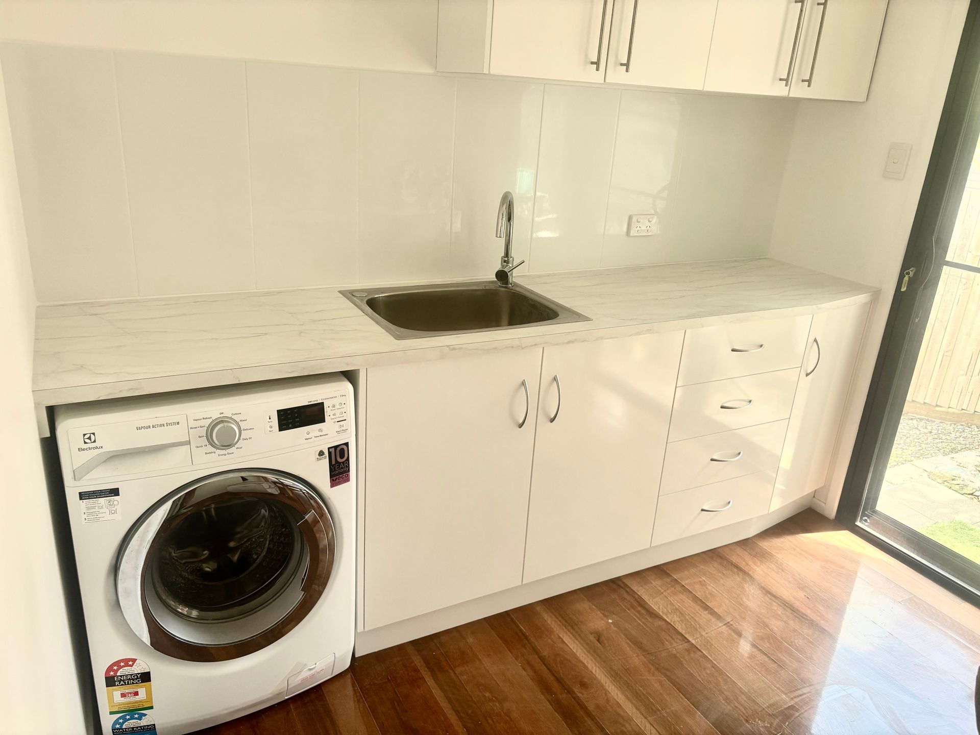 White Kitchen With Sink, Washing Machine, Cabinets, and Wooden Floor — RYDALL BUILDING AND DEVELOPMENT in Freshwater, QLD