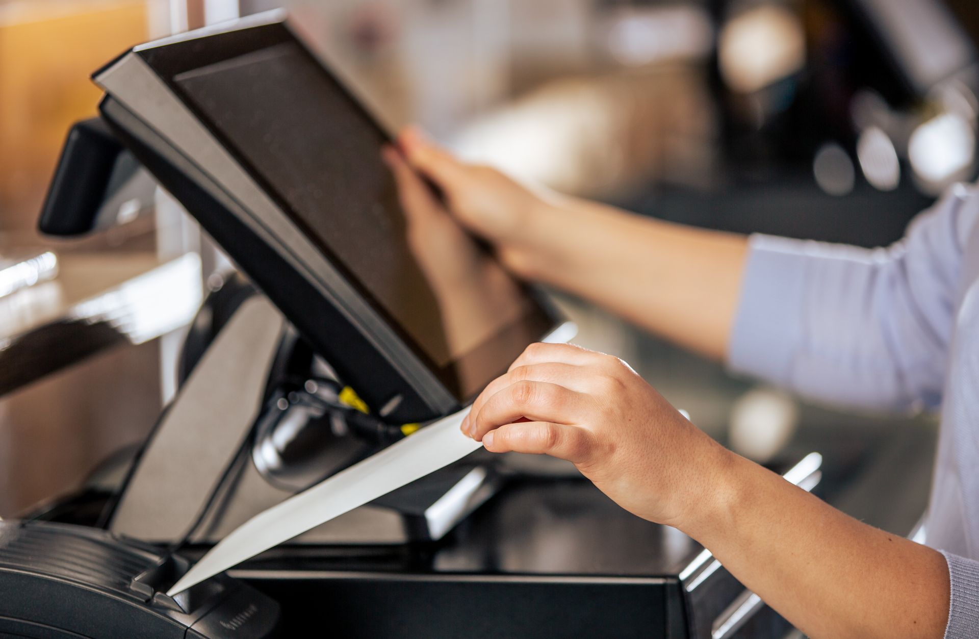Person holding a credit card near a touchscreen payment terminal at a checkout counter Person holding a credit card near a touchscreen payment terminal at a checkout counter