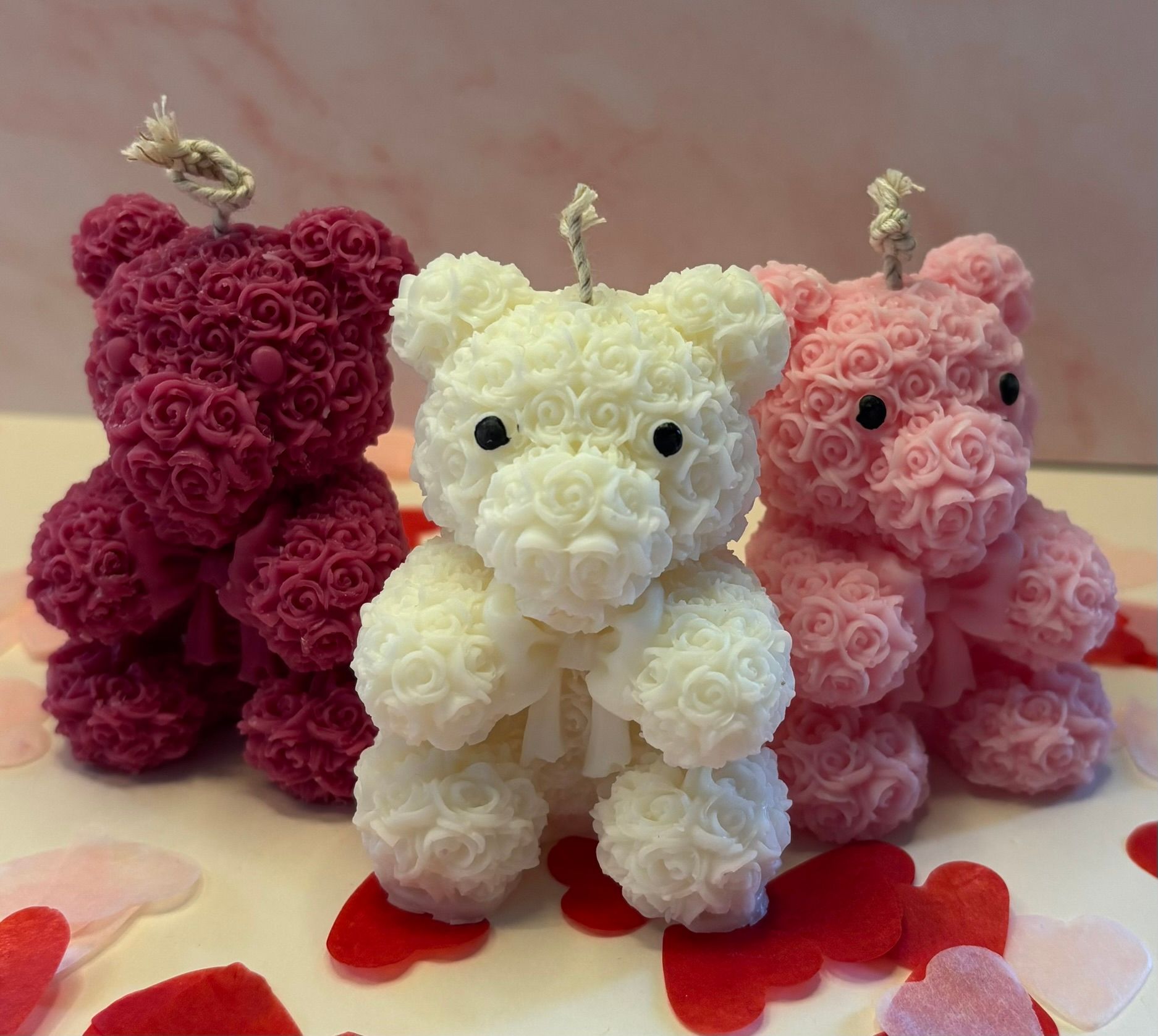 Drie kleine, met bloemen bedekte teddyberen in rood, wit en roze op een tafel met hartvormige versieringen.