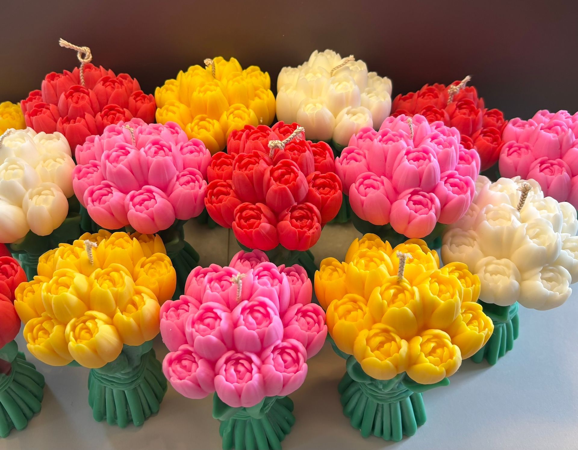 Een groepje kaarsen in de vorm van een tulpenboeket, in verschillende kleuren zoals geel, roze, rood en wit, is op een oppervlak gerangschikt.