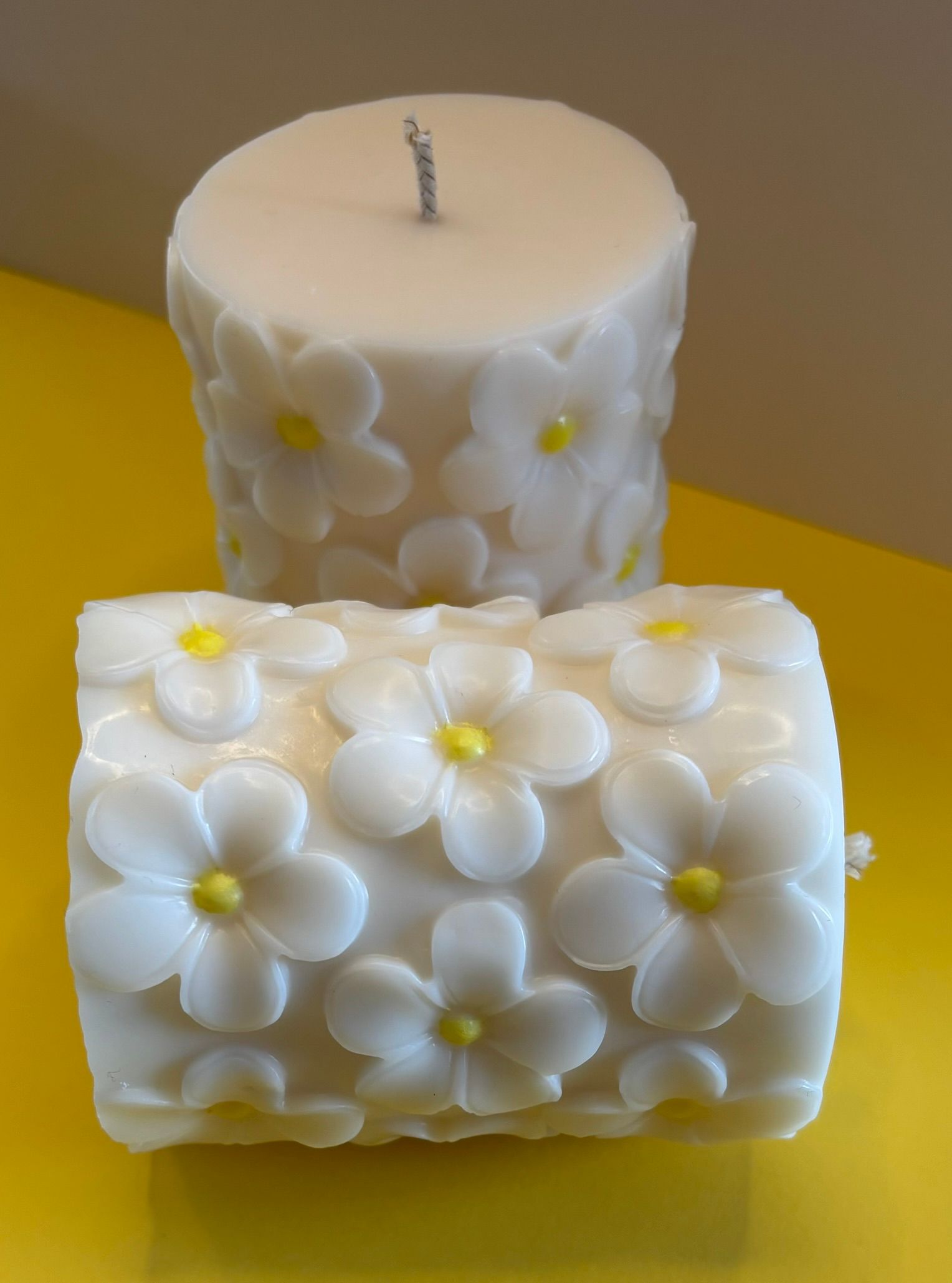 Drie witte kaarsen met bloemmotief op een gele ondergrond, met één kaars in het midden vooraan.