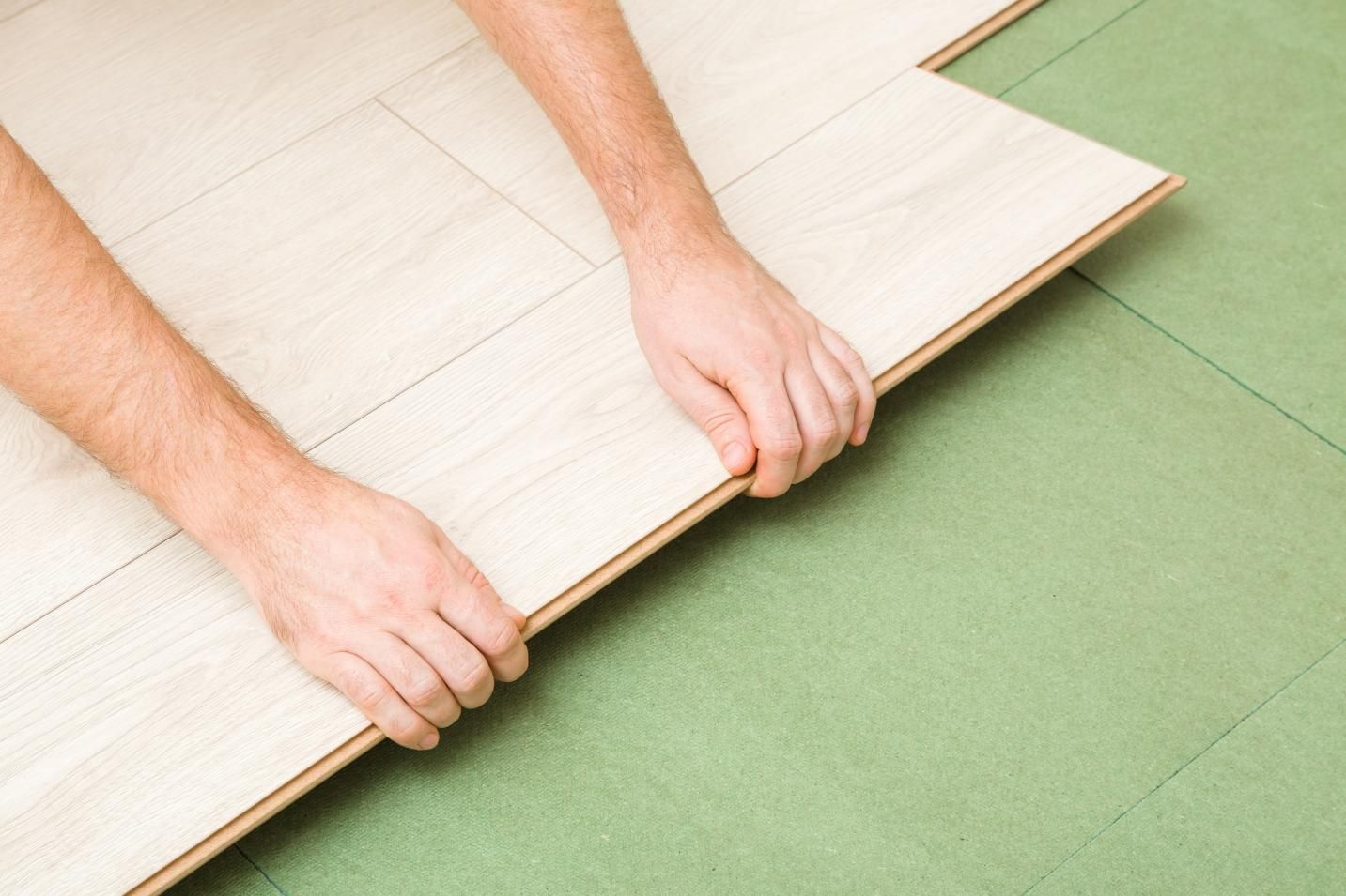 A Person is Laying a Piece of Hardwood Flooring on a Green Mat — Taggerts Discount Carpets & Vinyls In California Gully, VIC