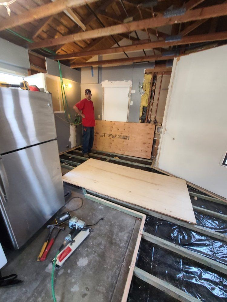 A man in a red shirt is standing next to a stainless steel refrigerator in a room under construction.