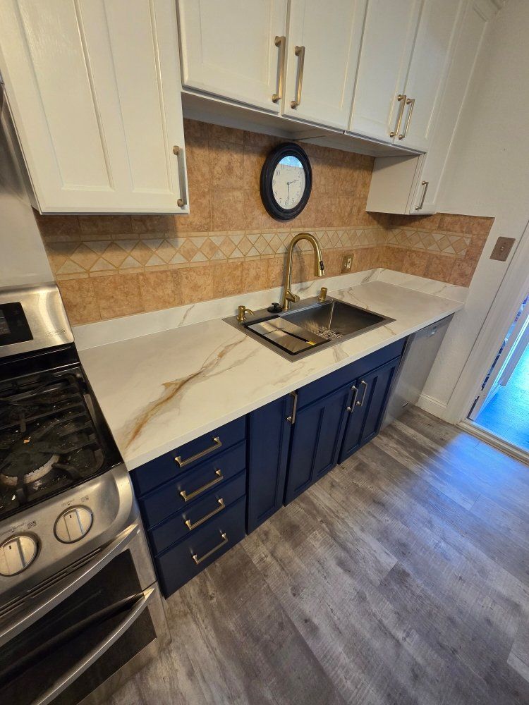 A kitchen with blue cabinets , a stove , a sink and a clock on the wall.