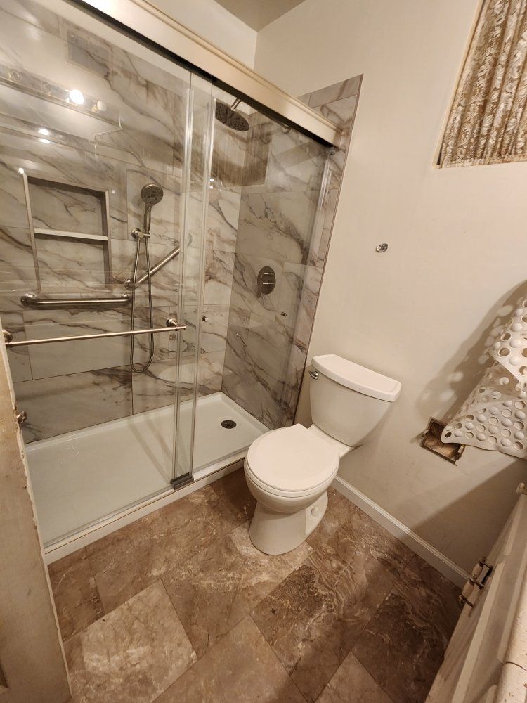 A bathroom with a toilet , shower and sliding glass door.