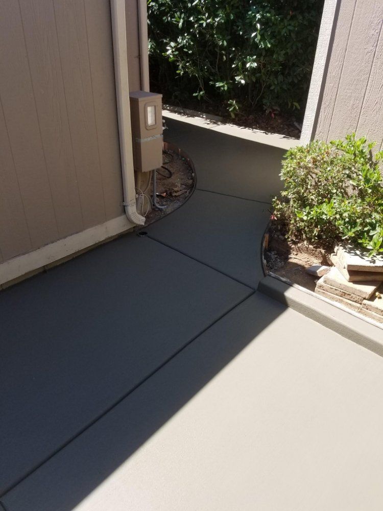 A concrete walkway leading to a house with a box on the side of it