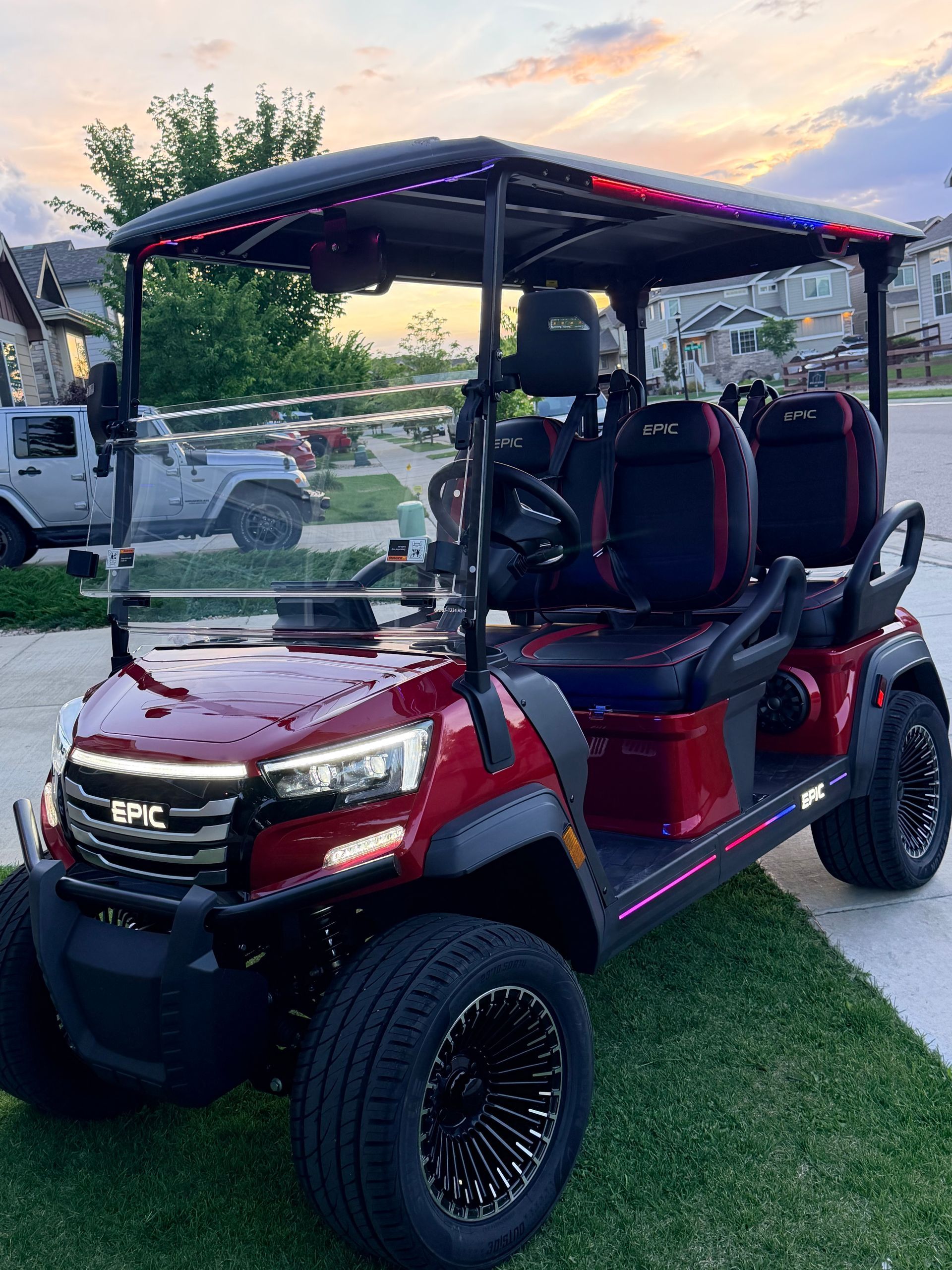 Red lifted golf cart with black roof and seats parked on grass at dusk.