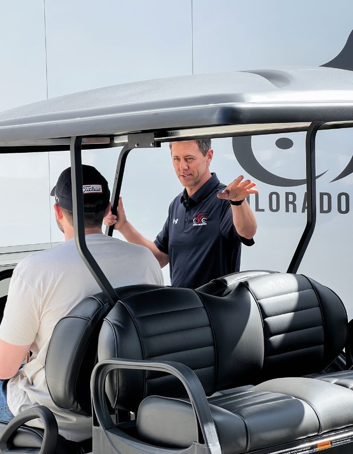 Two men beside a white aircraft, one sitting in a golf cart and one gesturing near the open door.