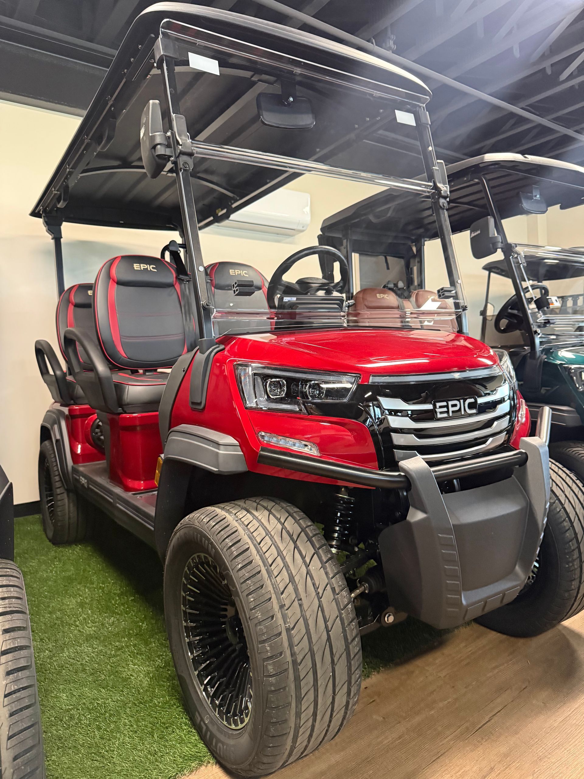 Red E-Z-GO golf cart with black roof and oversized tires displayed indoors on artificial turf.