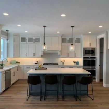 Modern white kitchen with large island, black stools, pendant lights, and built-in oven.