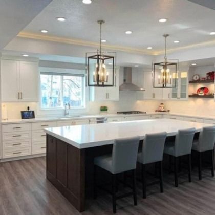 Bright modern white kitchen with large island, dark stools, pendant lights, and wood flooring