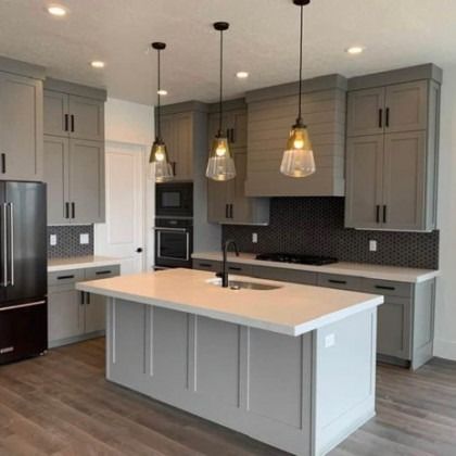 Modern kitchen with gray cabinets, white island, pendant lights, and dark wood flooring