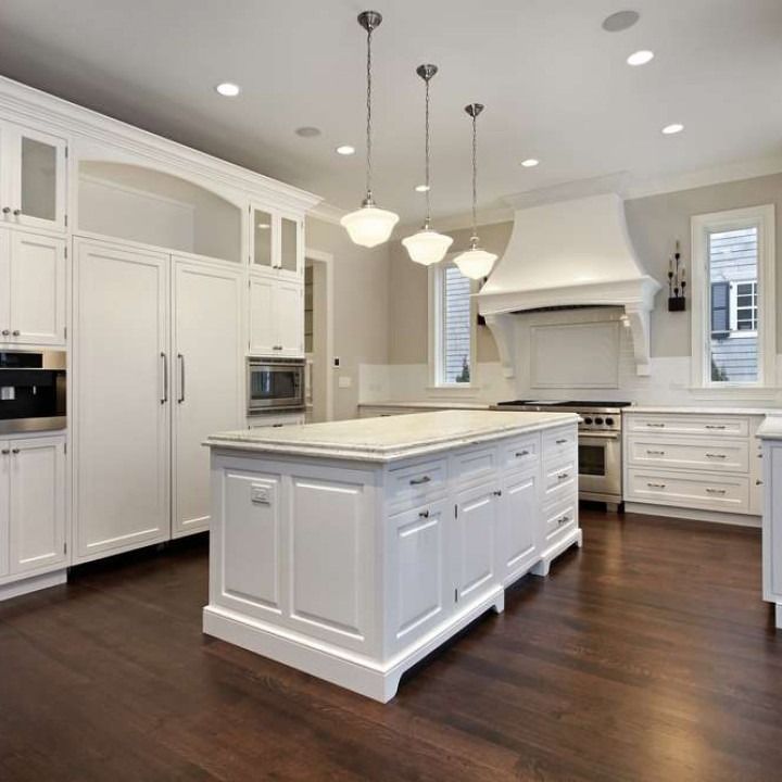 Bright white modern kitchen with a large island, dark wood floors, and pendant lights