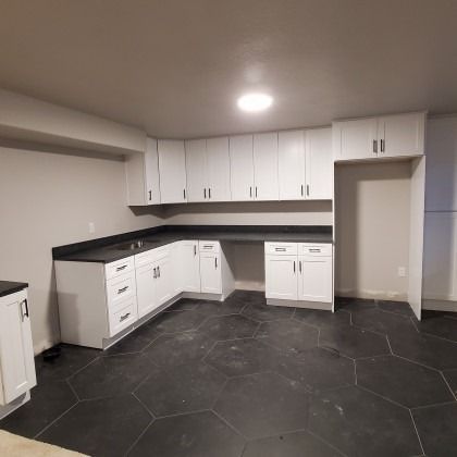 Empty modern kitchen with white cabinets, black countertops, and dark hexagon tile floor