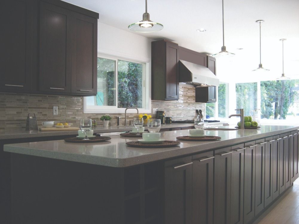 Modern kitchen with dark cabinets, large island, and bright windows overlooking greenery
