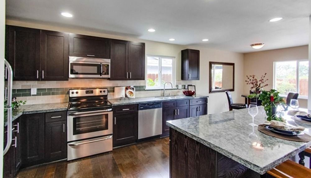 Modern kitchen with dark cabinets, stainless steel appliances, and a granite island countertop.