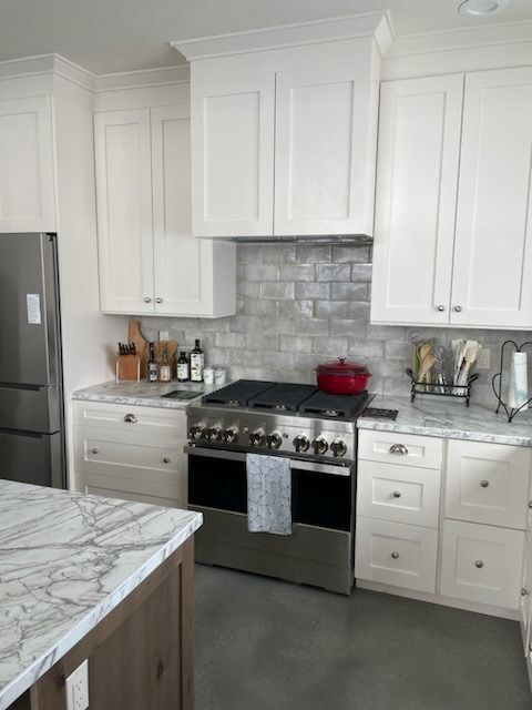 Bright white kitchen with marble island, stainless steel stove, and gray tile backsplash