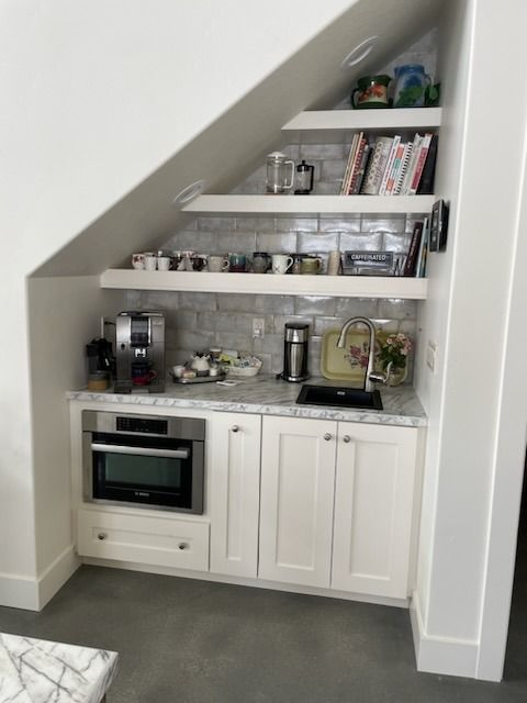 Built-in kitchen nook with white shelves, cabinets, and a small oven under a sloped ceiling