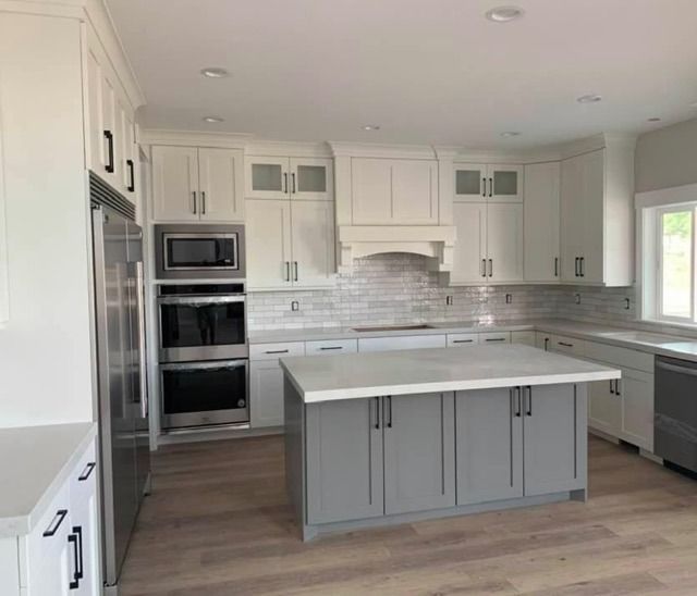 Bright modern kitchen with white cabinets, gray island, stainless appliances, and wood-look floors