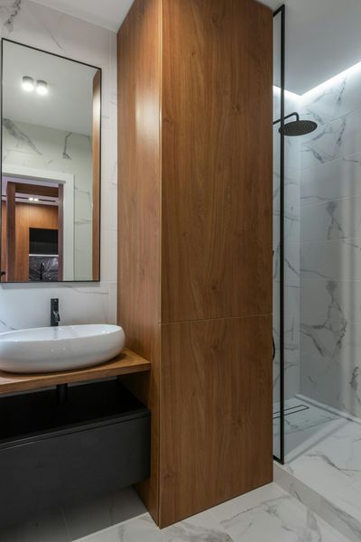 Compact bathroom with wood vanity cabinet, round sink, mirror, and glass shower enclosure