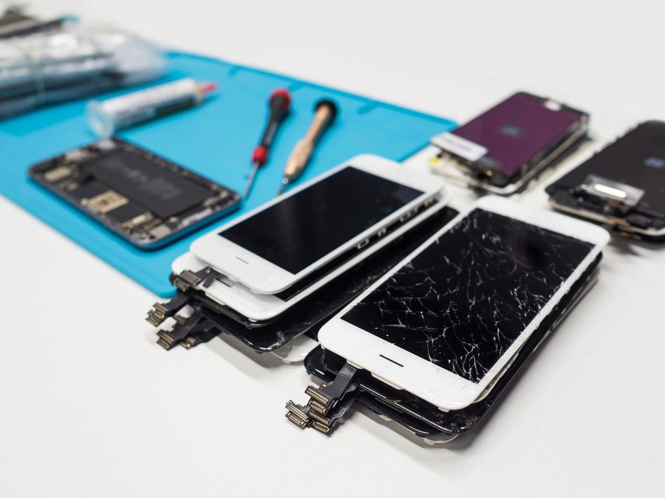 Smartphone smontati con schermi rotti su un tappetino di riparazione blu e relativi strumenti.