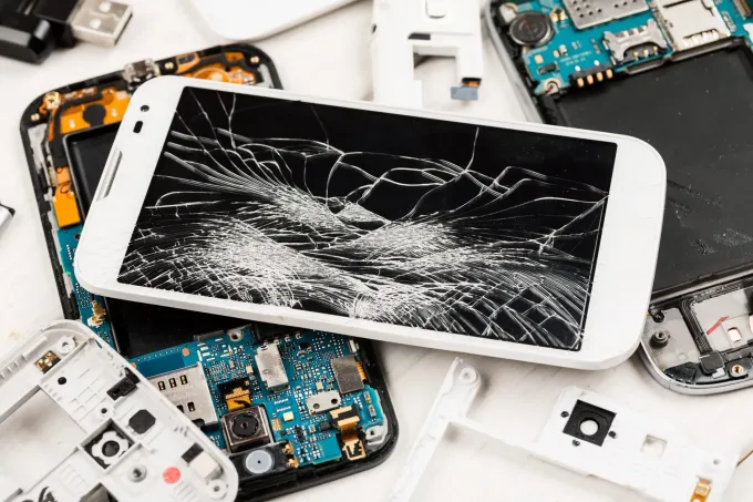 Smartphone rotto su un mucchio di apparecchi elettronici e componenti di telefoni danneggiati.