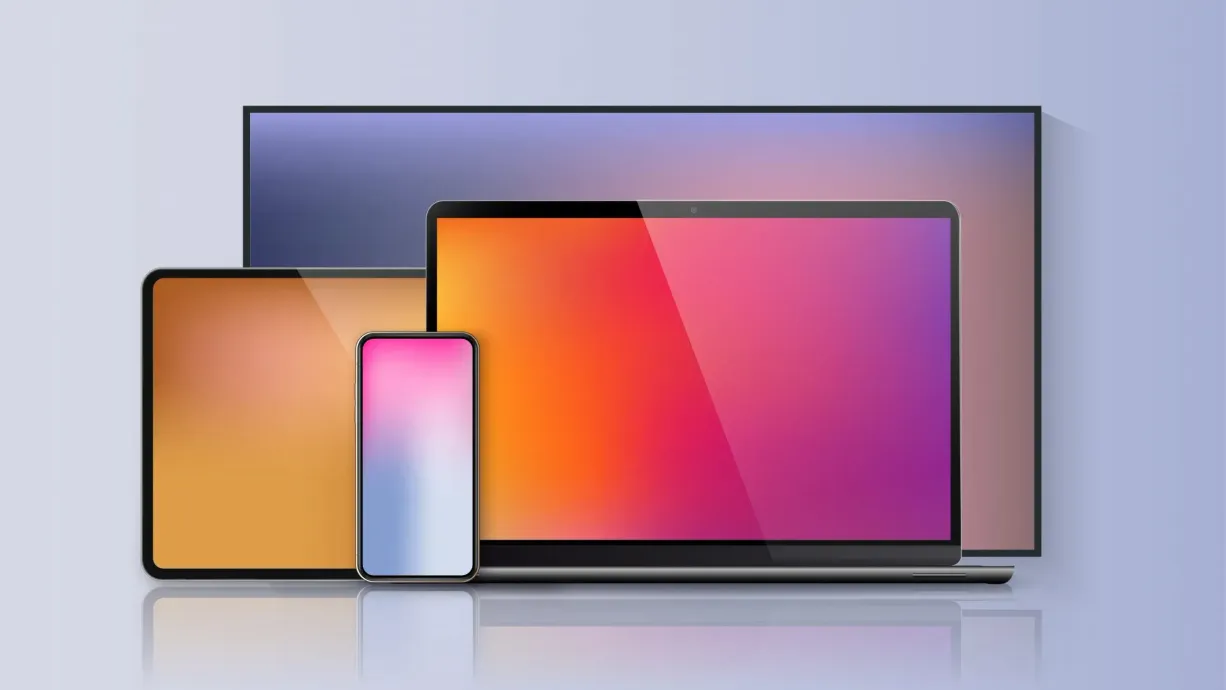 Due laptop e uno smartphone con schermi colorati sovrapposti davanti a un monitor più grande.