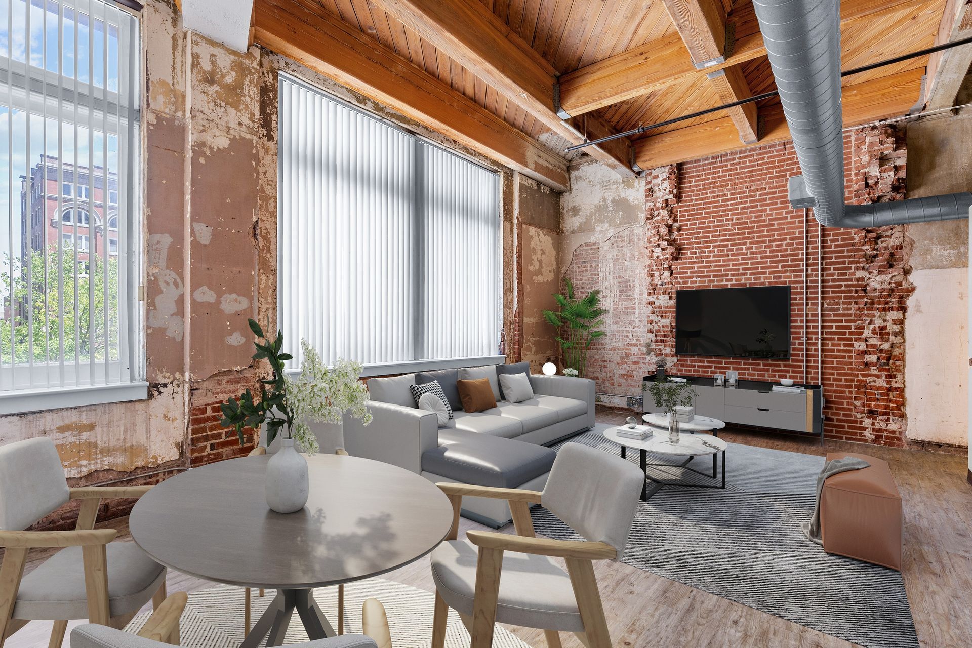 Modern loft living room with exposed brick, large windows, gray sofas, round table, and TV on the wall