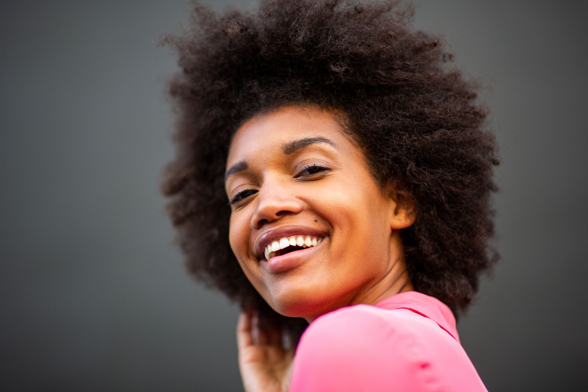 Une femme avec une afro sourit et regarde la caméra par-dessus son épaule.