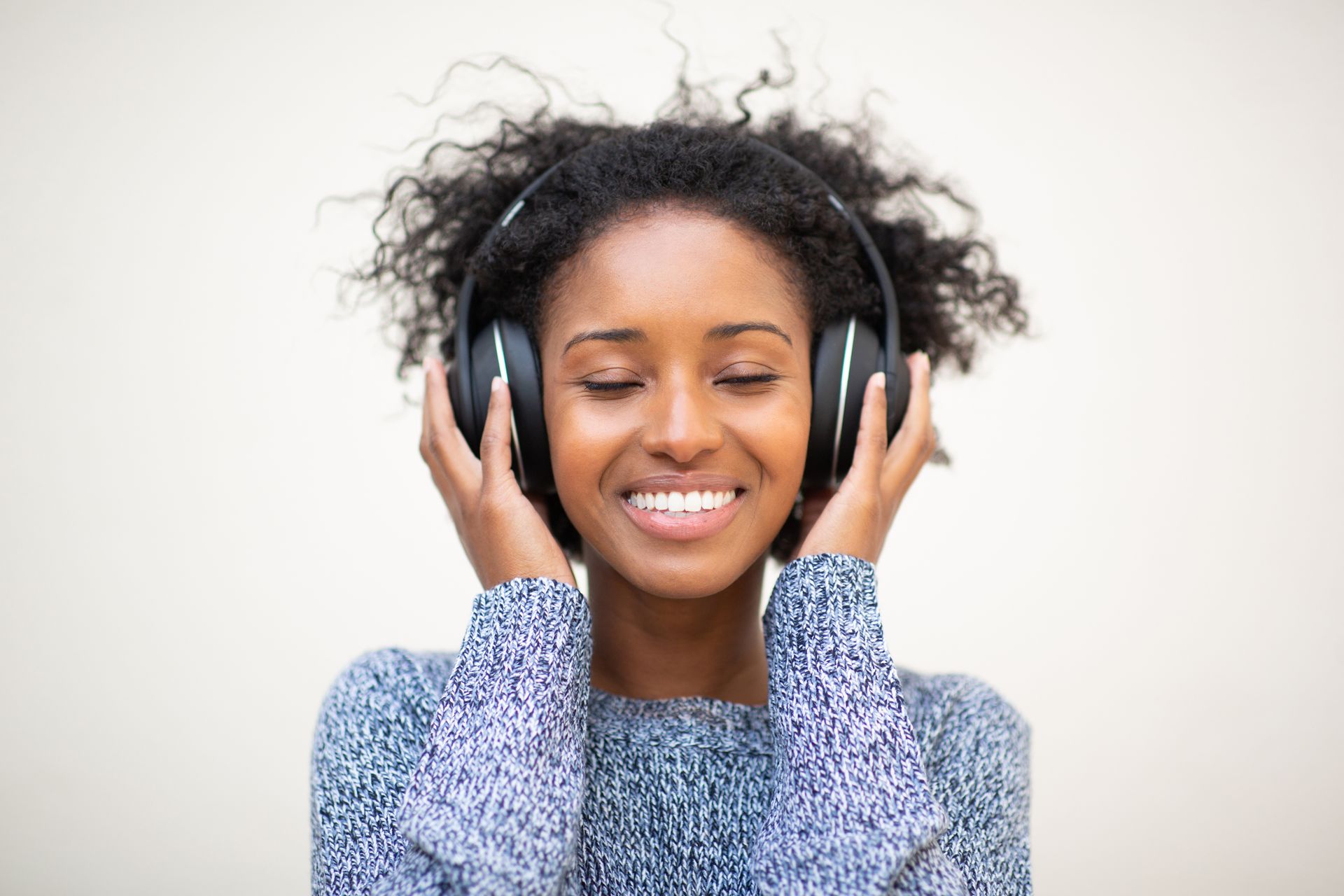 Une femme porte des écouteurs et sourit en écoutant de la musique.